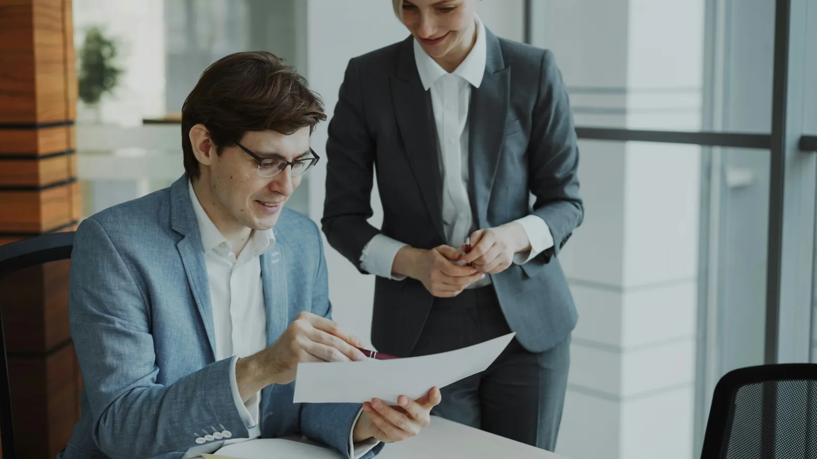 Two colleagues reviewing printed reports across a meeting table.